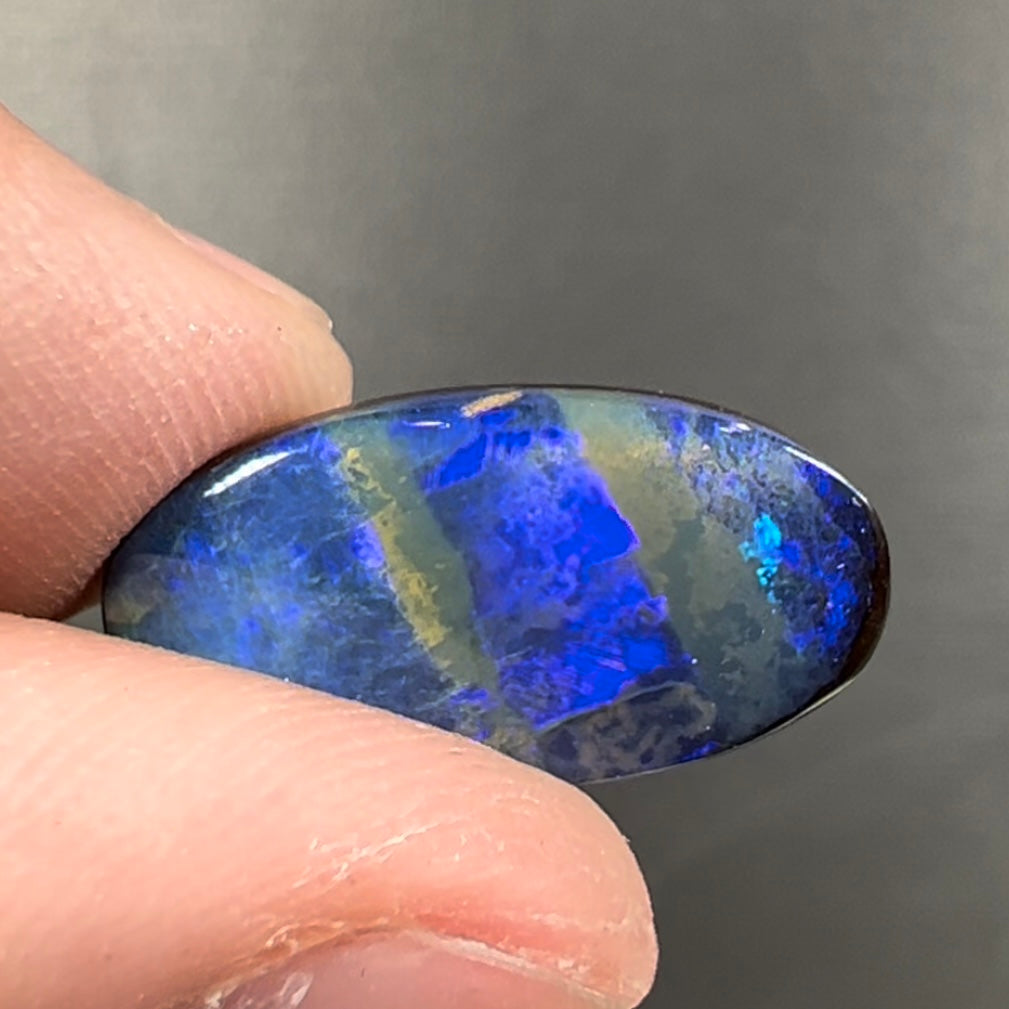 A loose, oval cabochon cut black boulder opal stone from Quilpie, Australia.