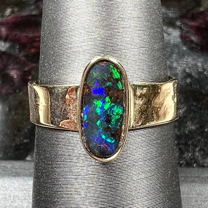 A blue green oval cabochon cut Australian boulder opal set in a yellow gold solitaire ring.