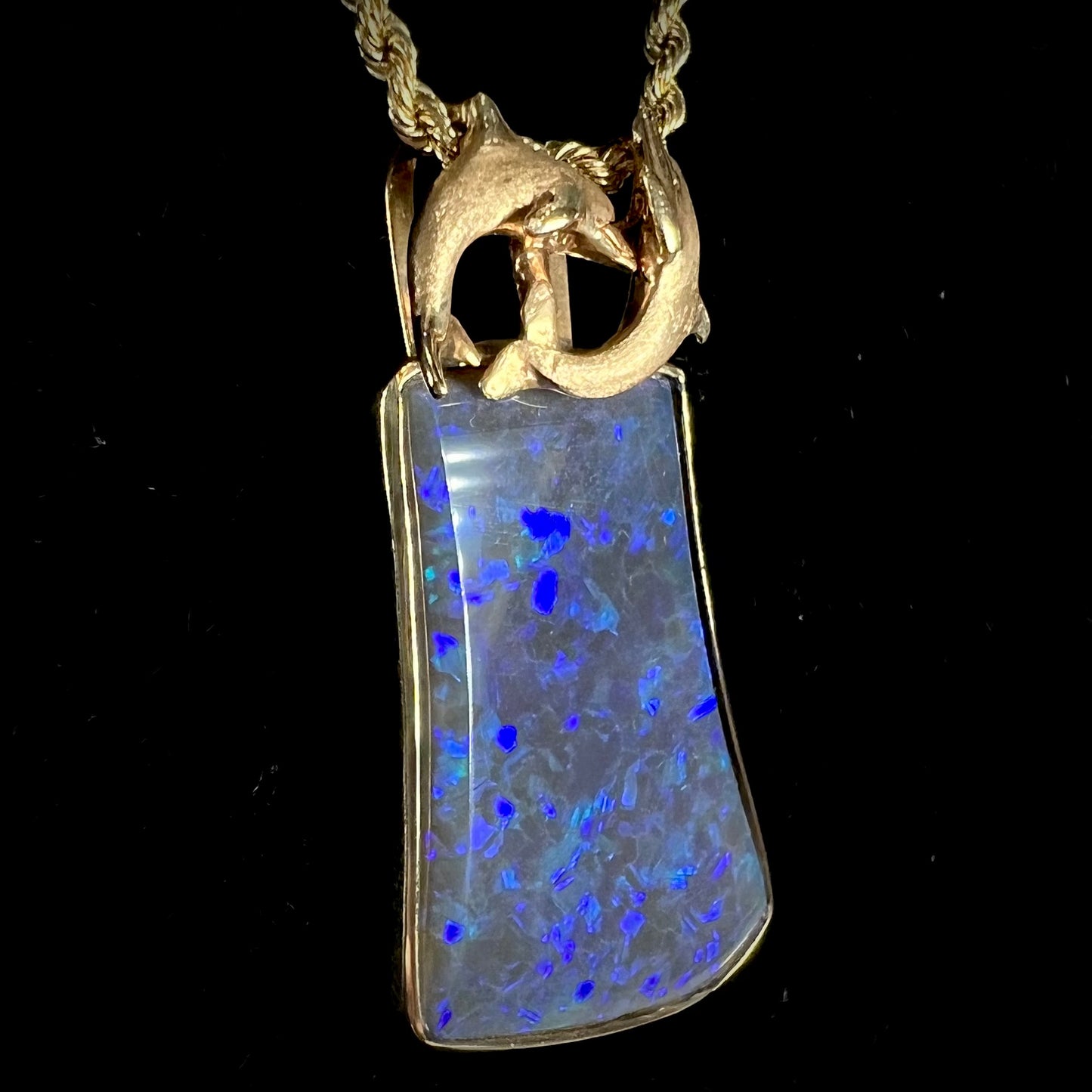 A gold freeform cut black opal bezel pendant cast with two dolphins on top of the opal.