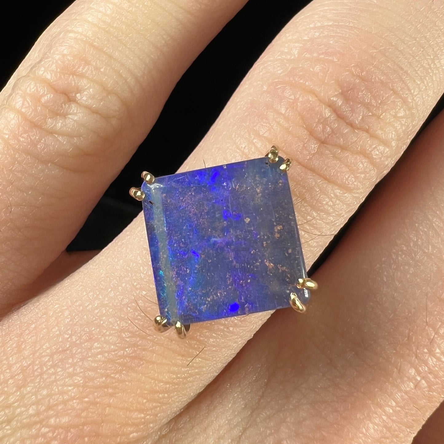 A ladies' boulder opal solitaire ring, handmade in yellow gold.  The stone is purple with flashes of blue, aqua, and green.