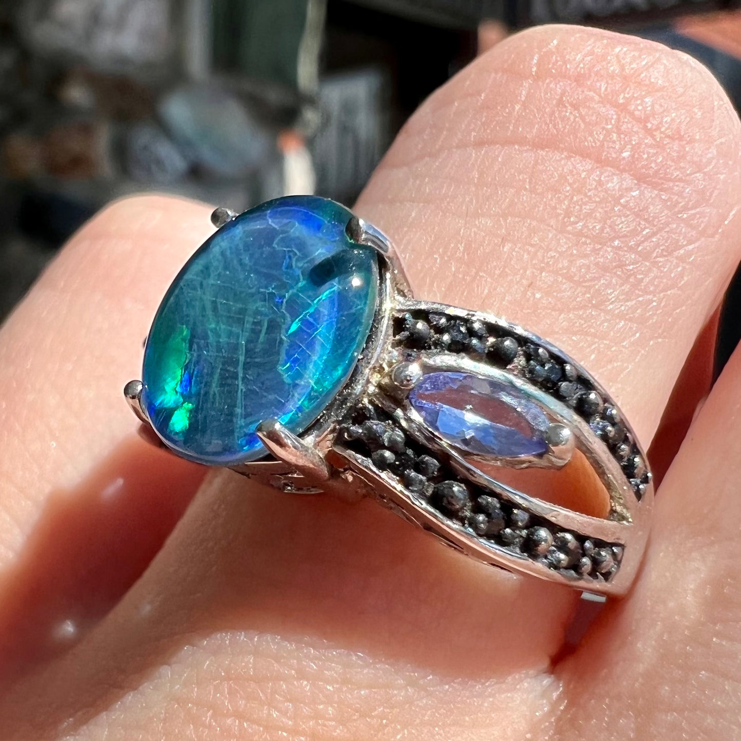 A sterling silver ring set with a black opal triplet, two marquise cut tanzanites, and round black spinel accent stones.