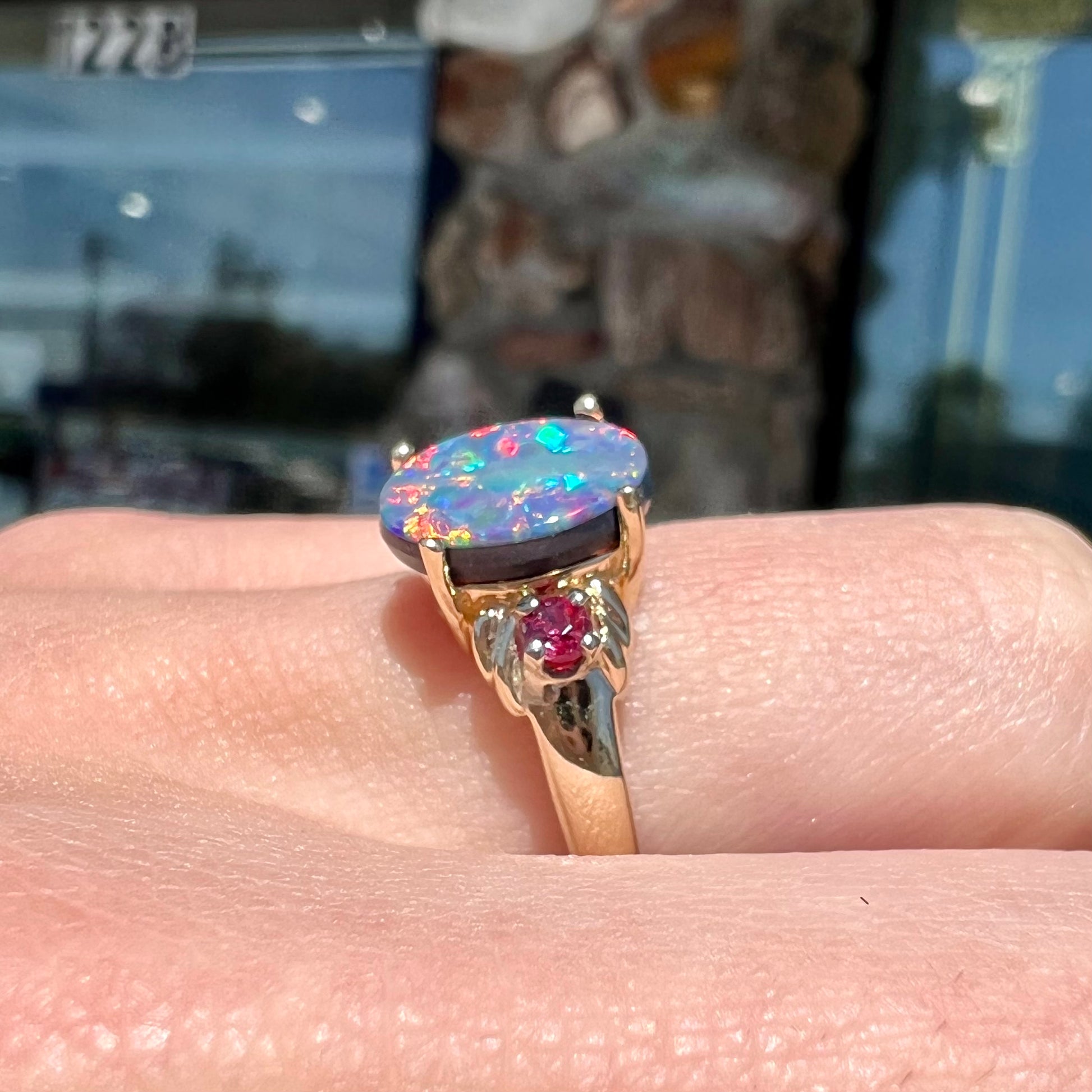 A yellow gold ring prong set with a black opal doublet cabochon and two round ruby accents.