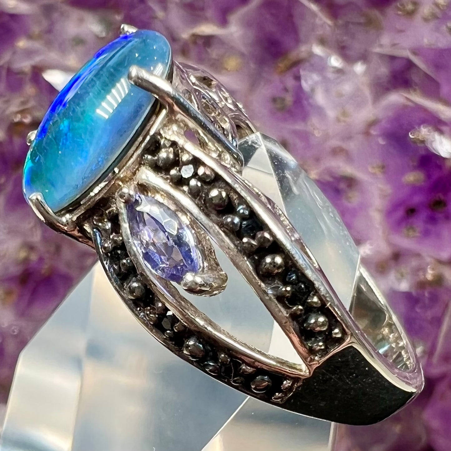 A sterling silver ring set with a black opal triplet, two marquise cut tanzanites, and round black spinel accent stones.