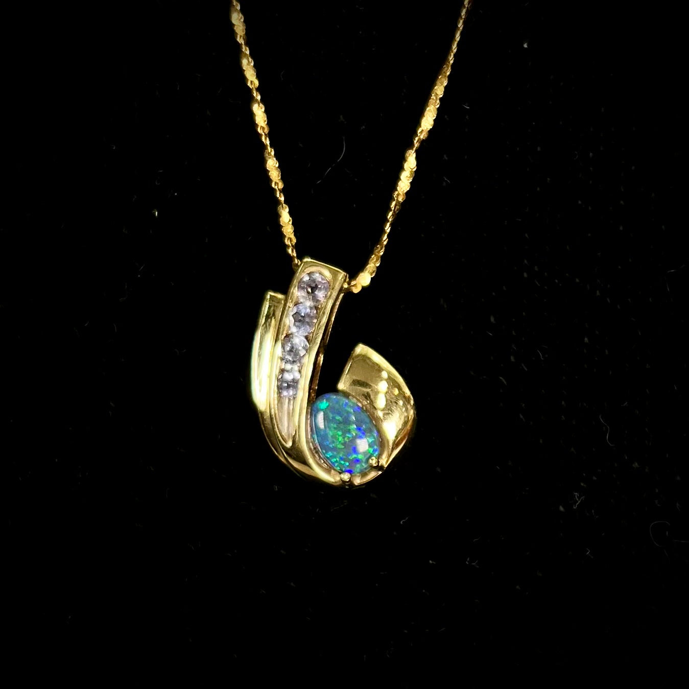 A Lightning Ridge black crystal opal necklace set with blue tanzanite in yellow gold.  Gold chain not included.