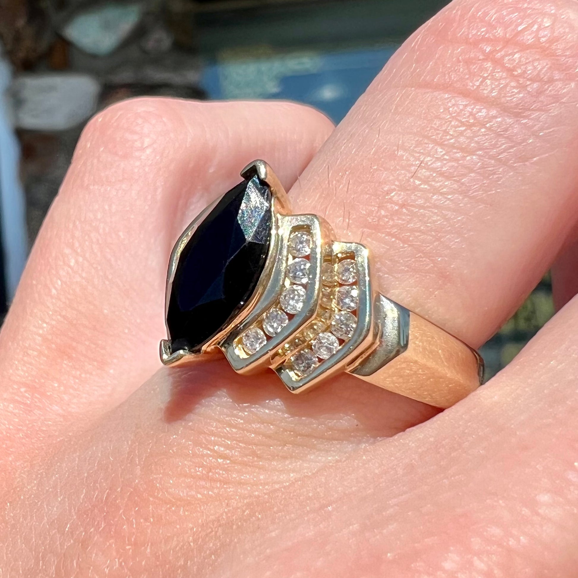 A gold, marquise cut black sapphire ring set with channel set diamond accents.