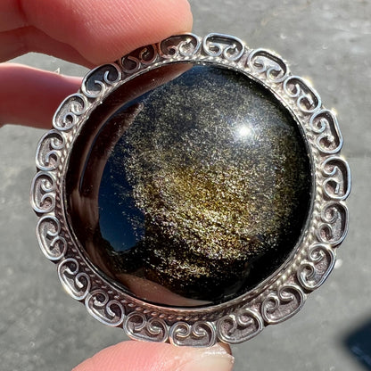A sterling silver pendant/brooch bezel set with a round cabochon cut black sheen obsidian stone.