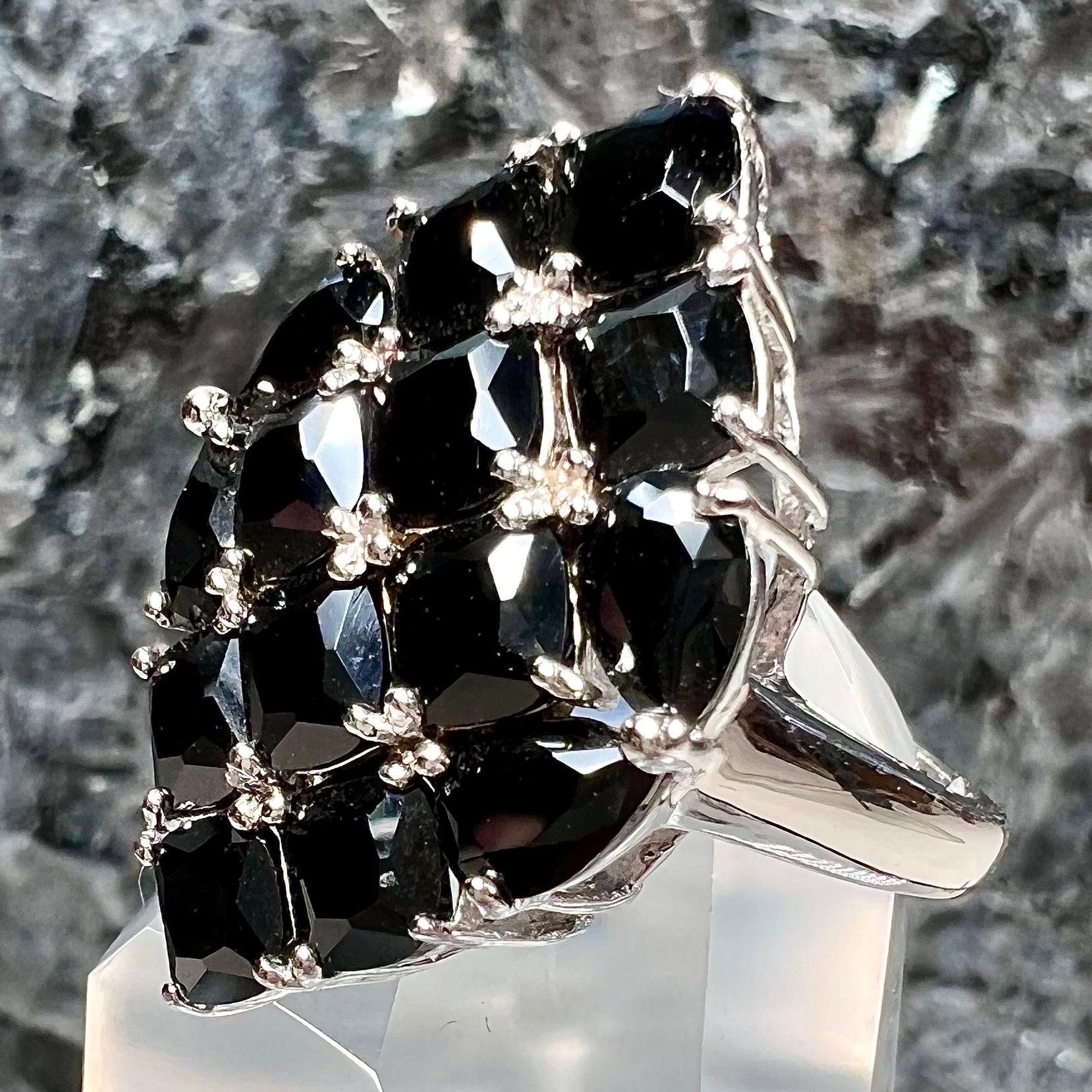A sterling silver ring cluster set with faceted black spinel stones set to form a marquise shape.