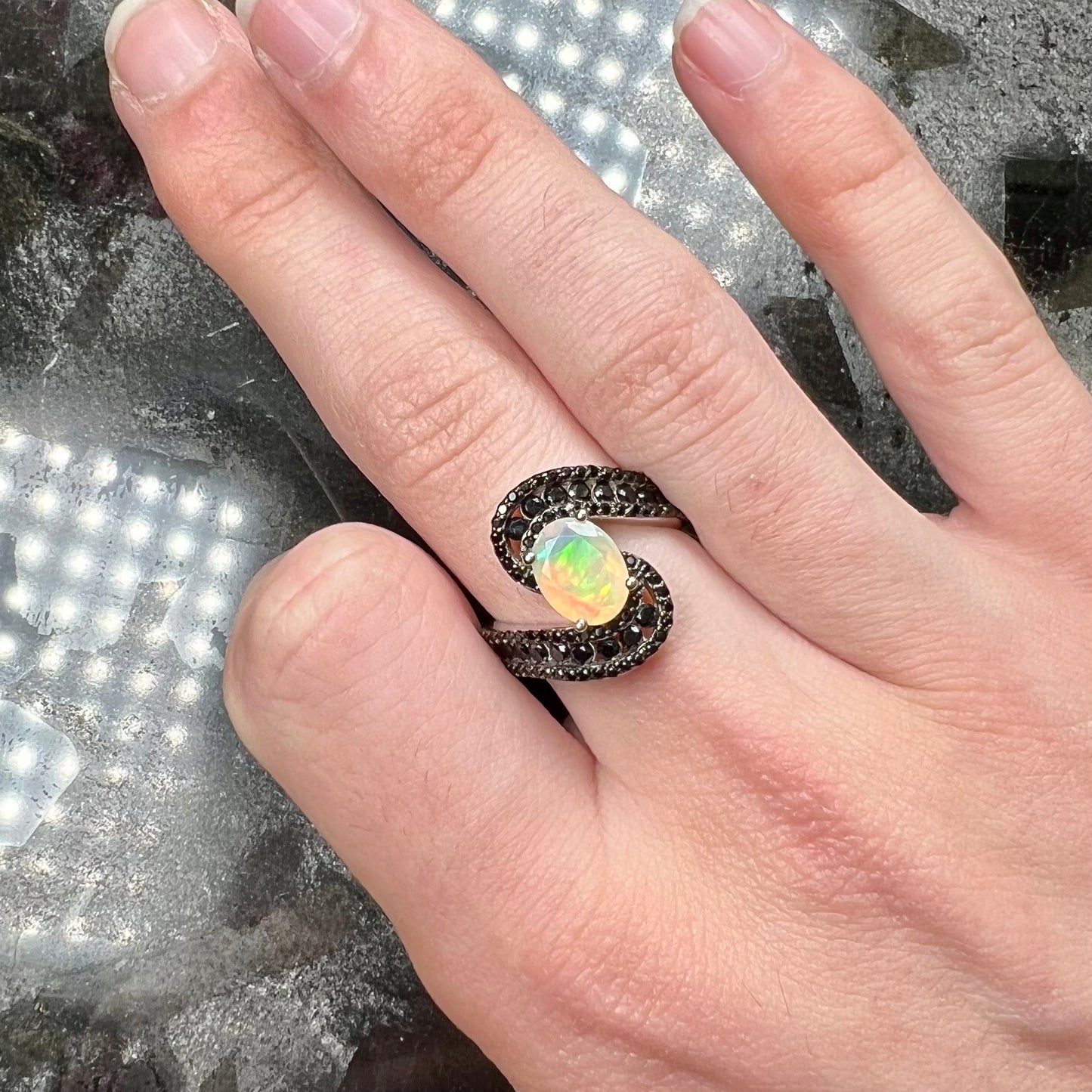 A sterling silver ring set with round black spinel stones and an oval cut, faceted Ethiopian opal.