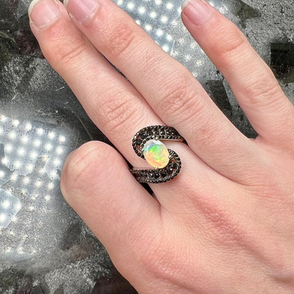 A sterling silver ring set with round black spinel stones and an oval cut, faceted Ethiopian opal.