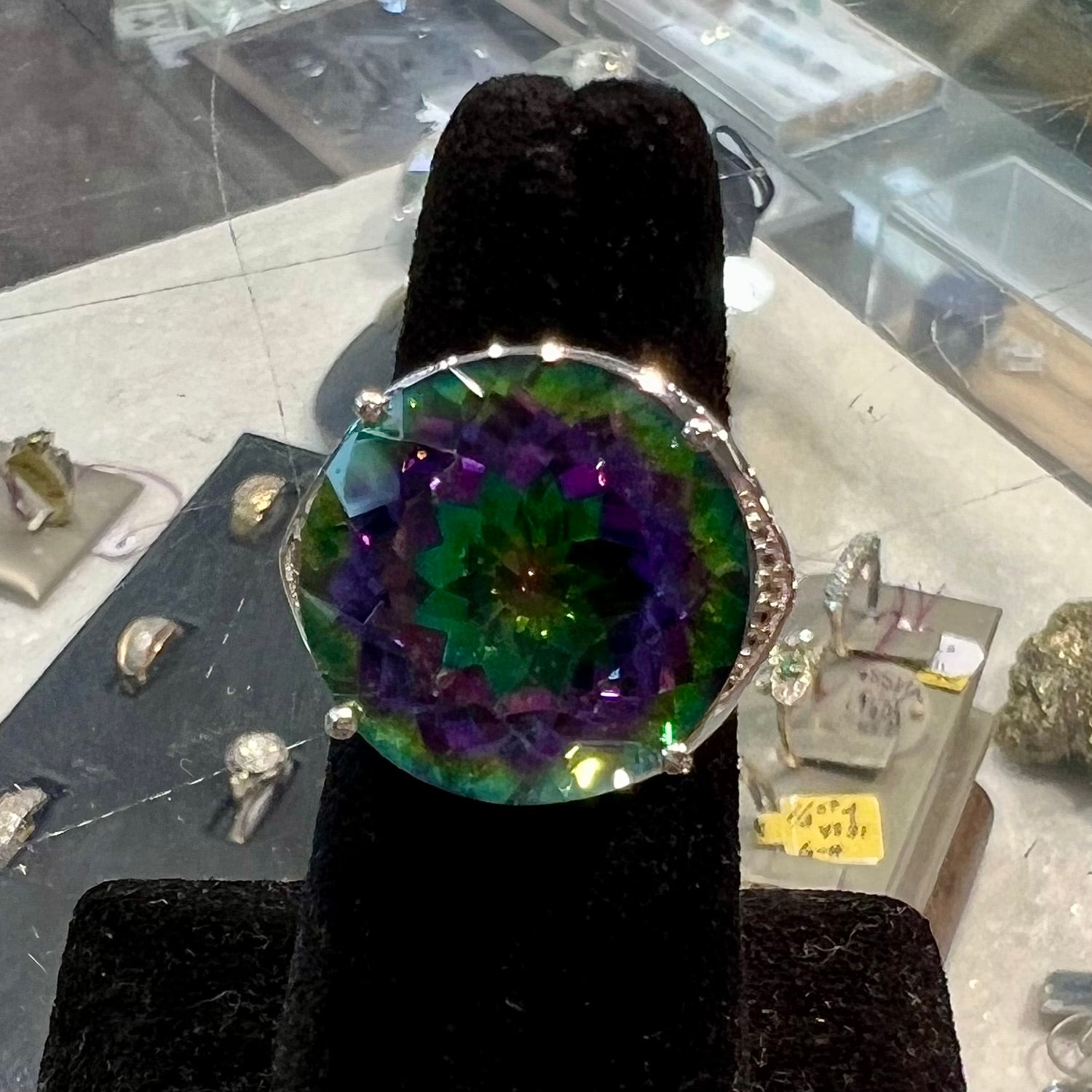 A large, round cut pink and green mystic topaz set in a sterling silver ring with white topaz accent stones.