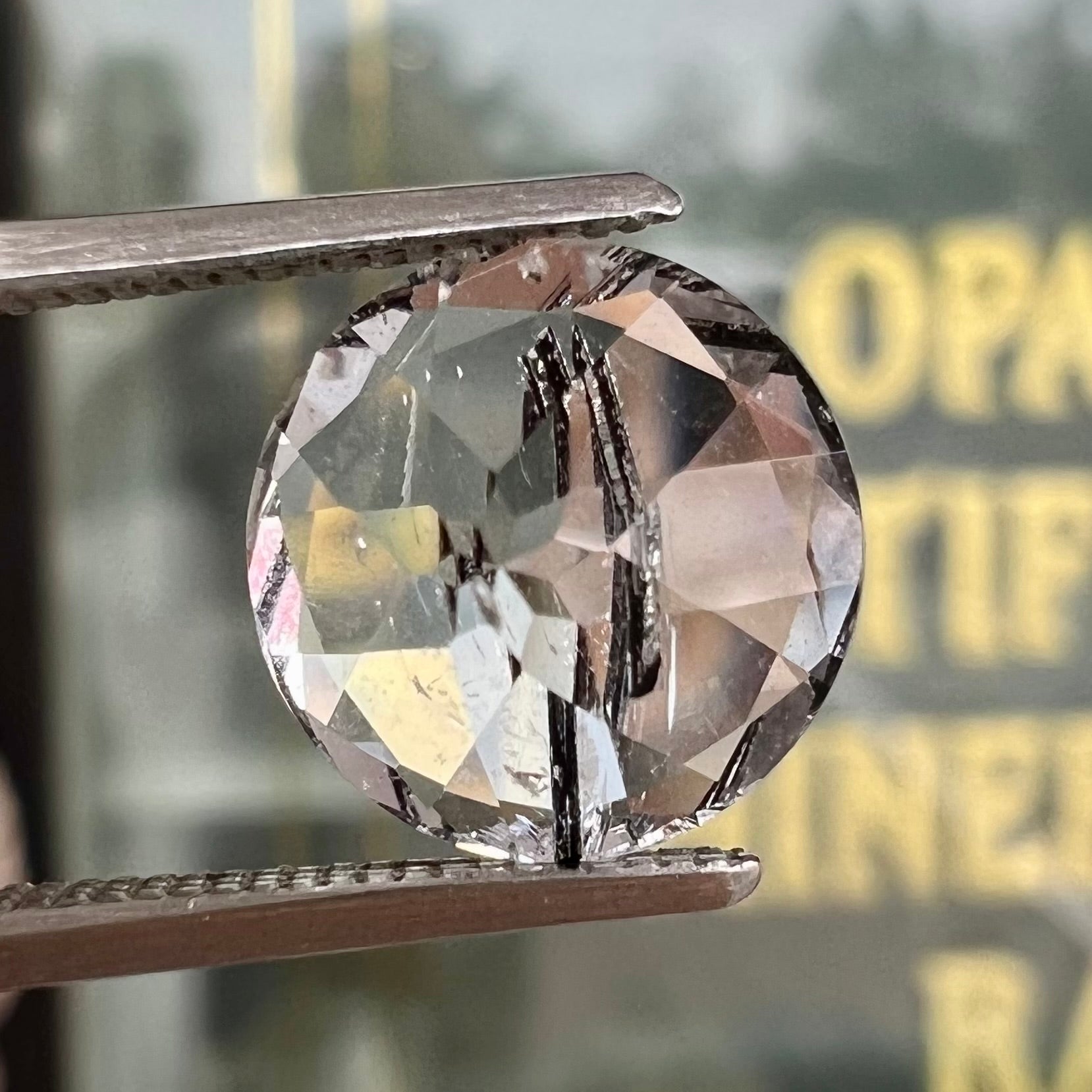 A faceted round brilliant cut clear quartz stone with black tourmaline inclusions.  Inclusions appear like a clock's hands.
