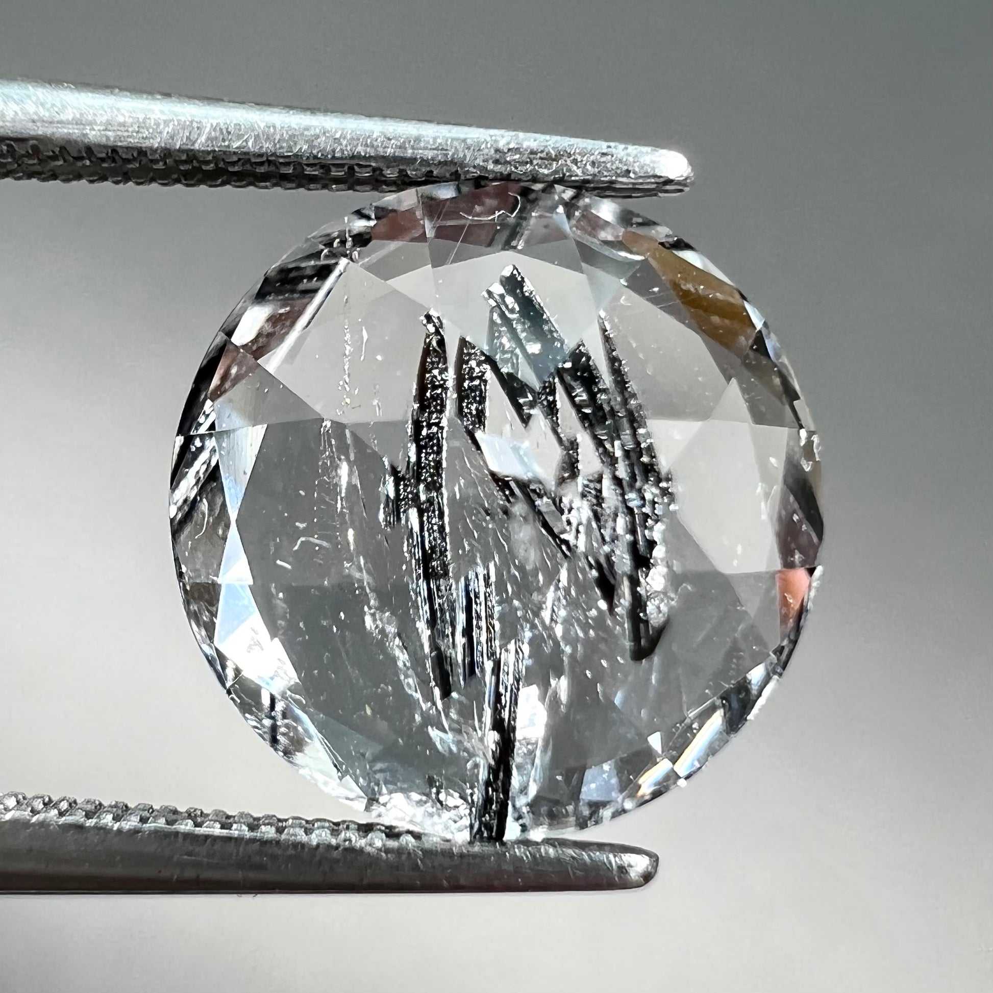 A round brilliant cut clear quartz stone with two black tourmaline crystal inclusions.