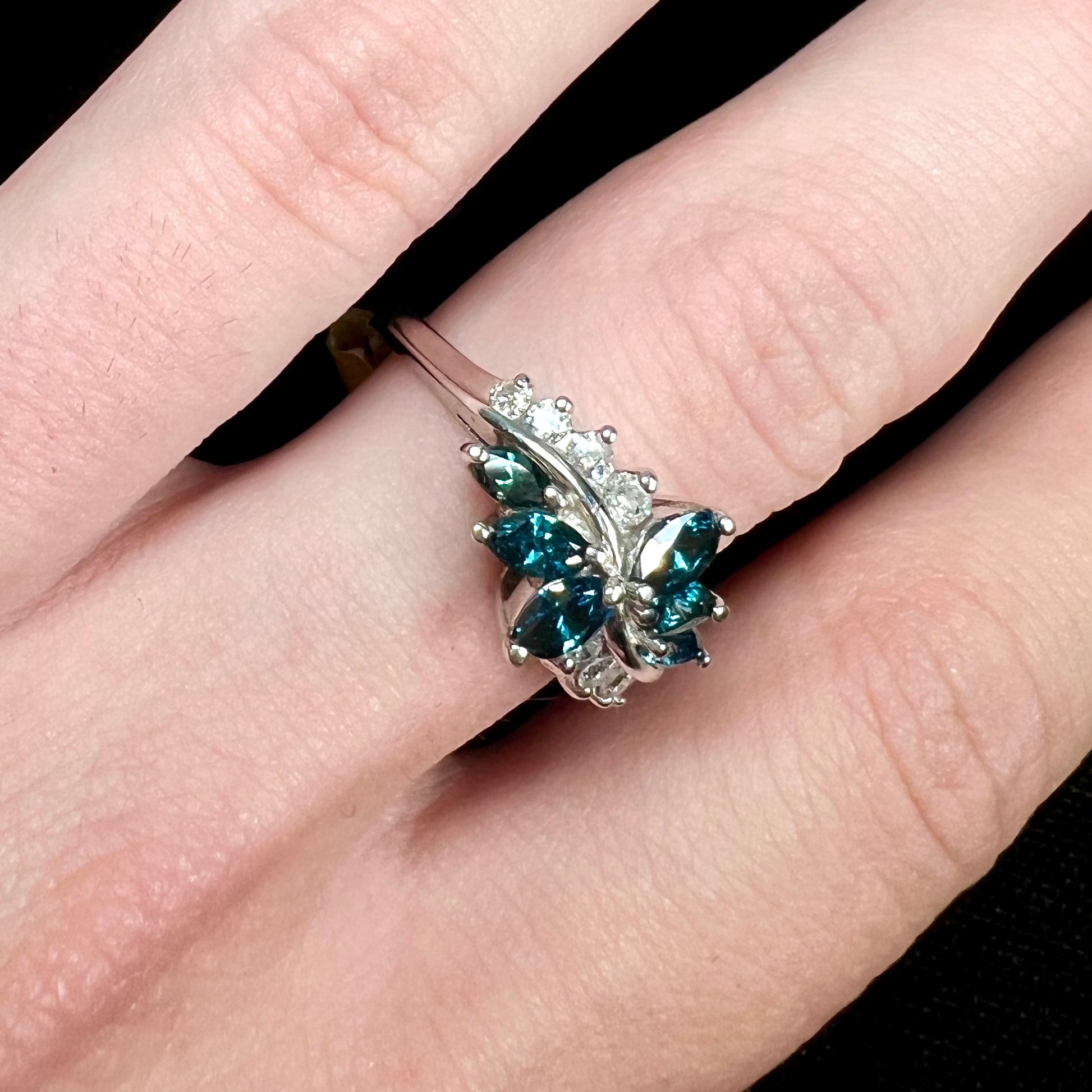 A white gold diamond cluster ring set with blue marquise cut and white round cut diamonds.