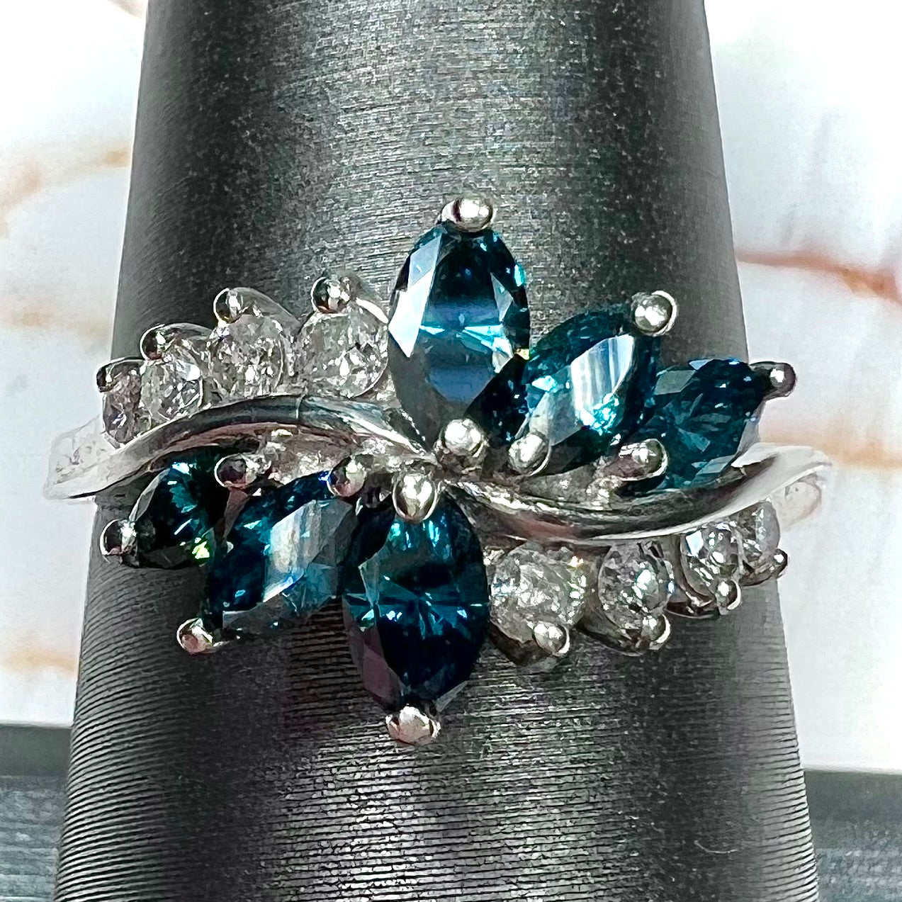 A white gold diamond cluster ring set with blue marquise cut and white round cut diamonds.