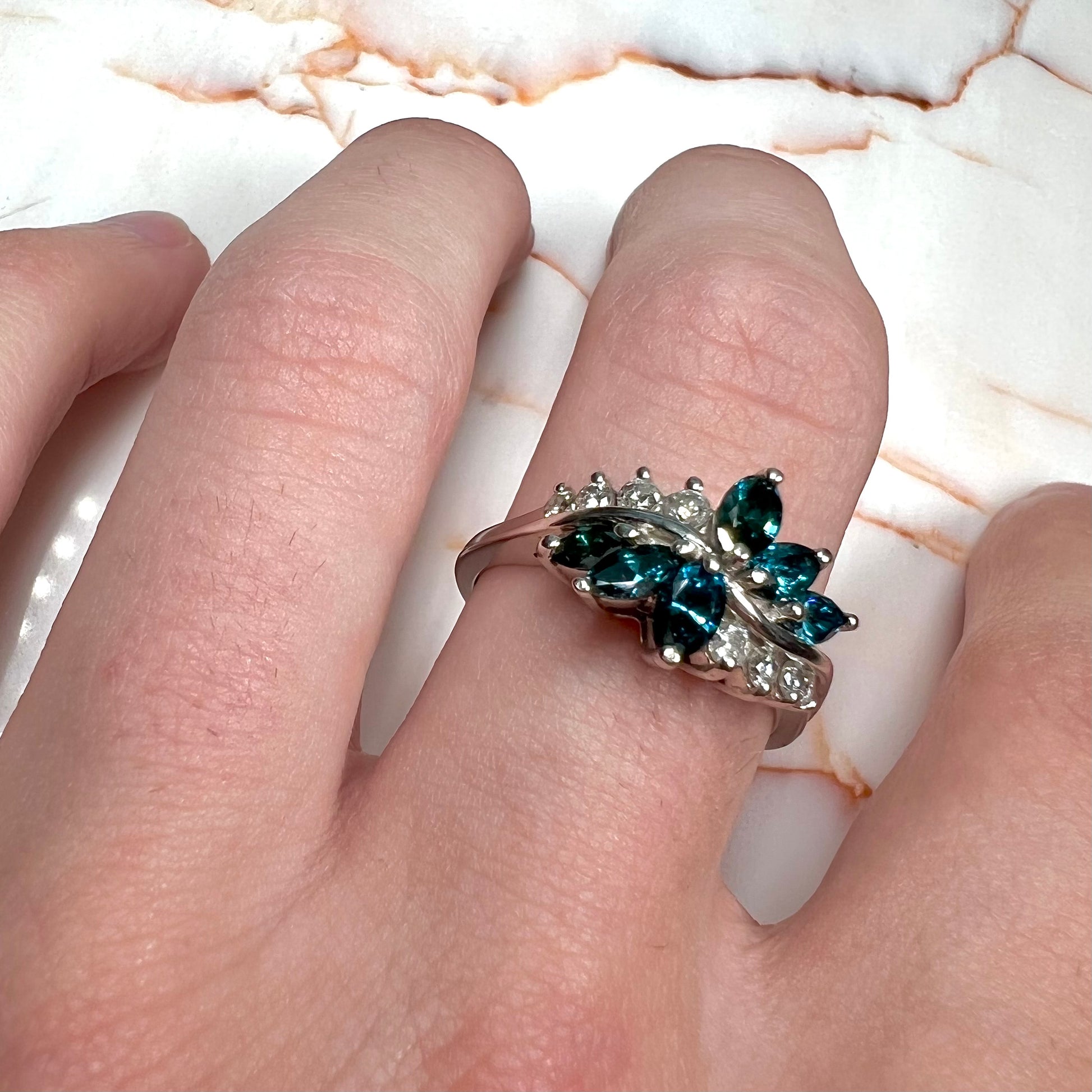 A white gold diamond cluster ring set with blue marquise cut and white round cut diamonds.