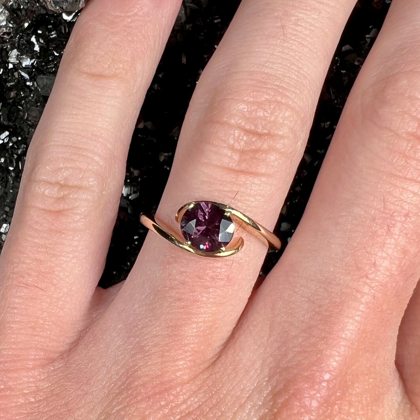 A yellow gold solitaire engagement ring set with a faceted oval cut color change garnet stone.