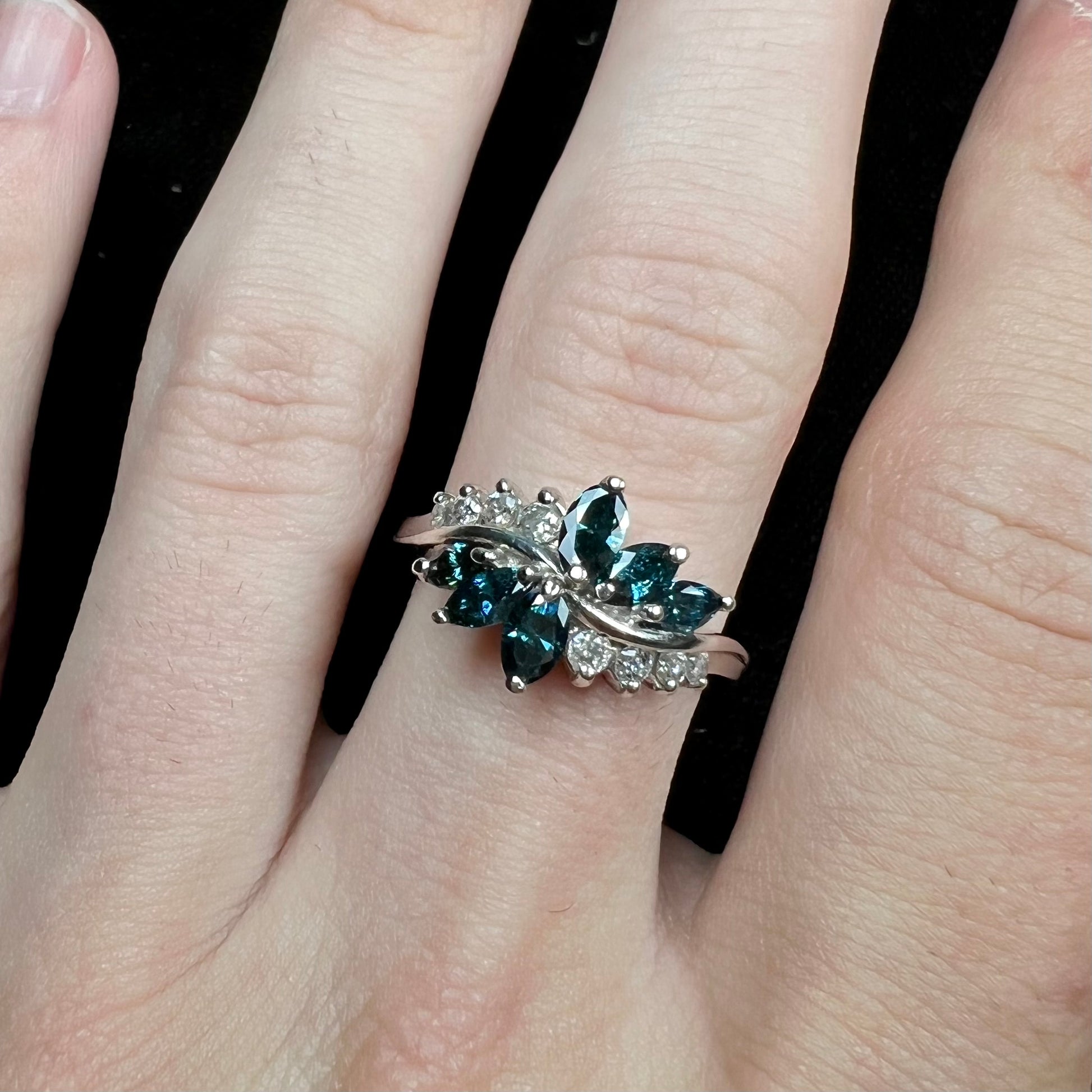 A white gold diamond cluster ring set with blue marquise cut and white round cut diamonds.