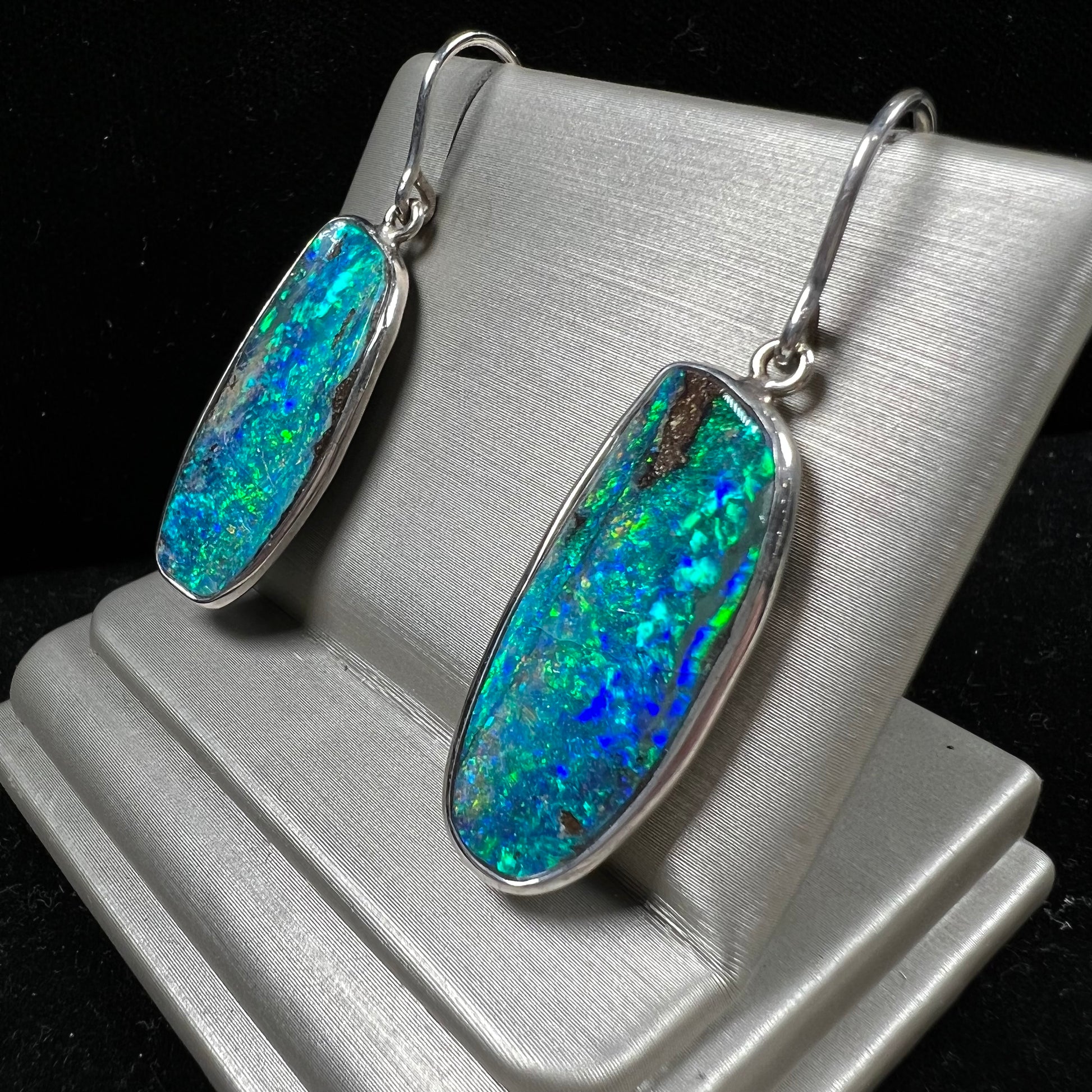 A pair of white gold boulder opal French wire dangle earrings.  The opal is predominantly glimmery blue.
