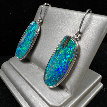 A pair of white gold boulder opal French wire dangle earrings.  The opal is predominantly glimmery blue.