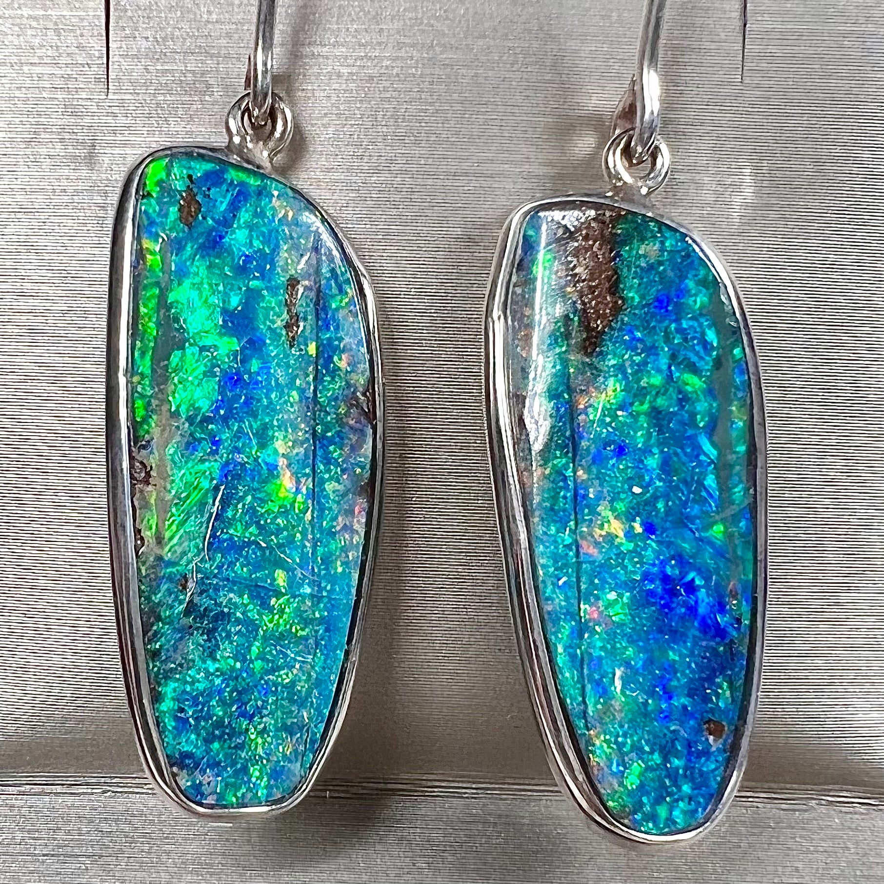 A pair of white gold boulder opal French wire dangle earrings.  The opal is predominantly glimmery blue.