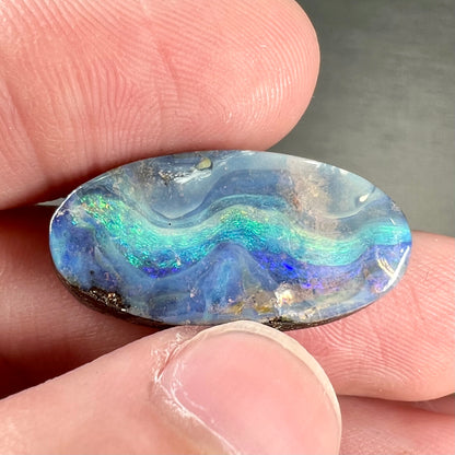 A loose, oval cabochon cut Quilpie boulder opal from Queensland, Australia.  The stone is blue with green fire.