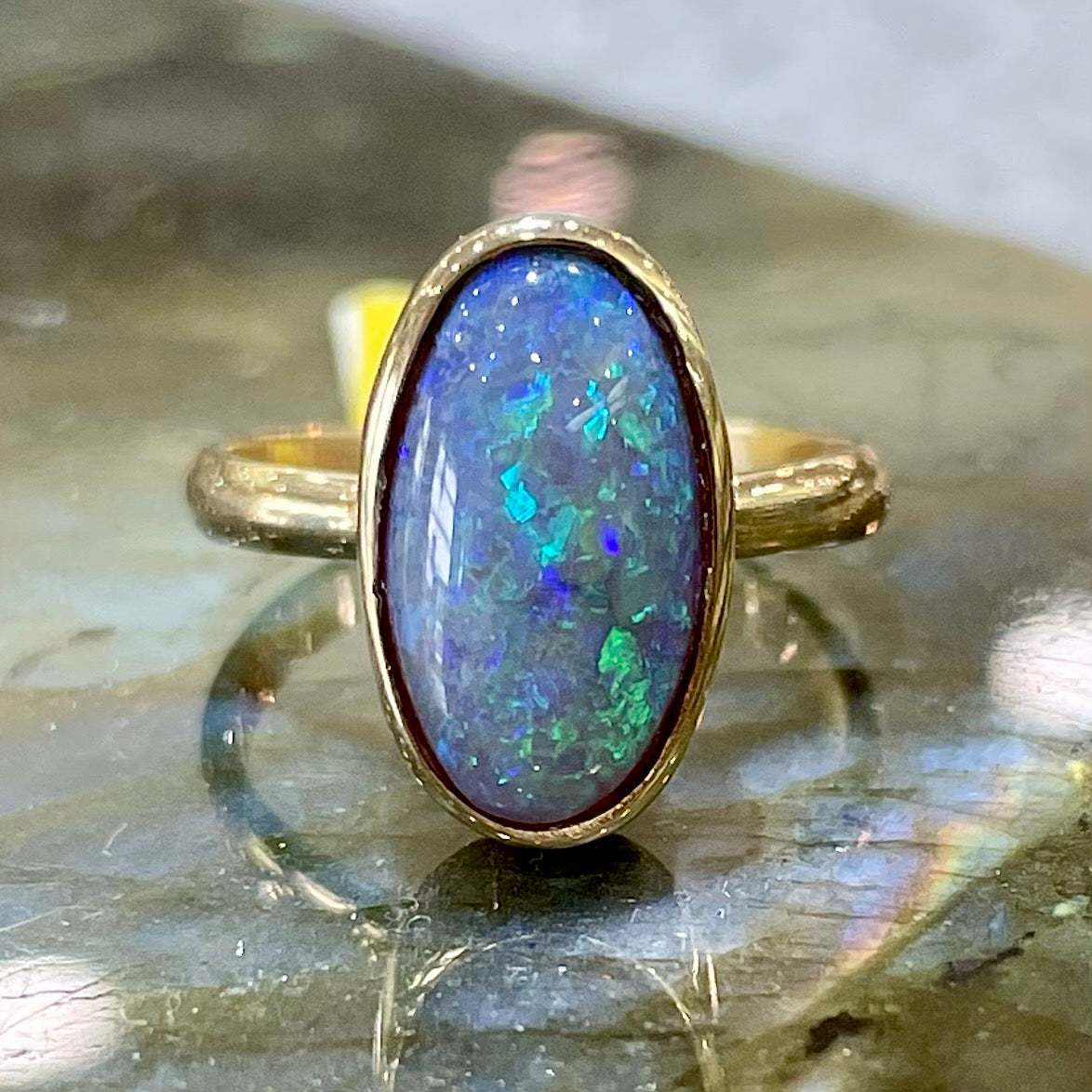 A simple yellow gold solitaire ring with a bezel set Lightning Ridge black crystal opal from Australia.