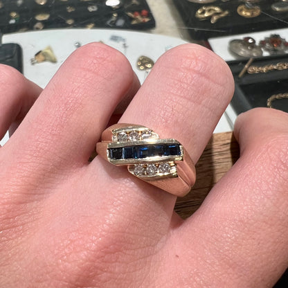 A men's yellow gold ring channel set with princess cut blue sapphires and diamonds.