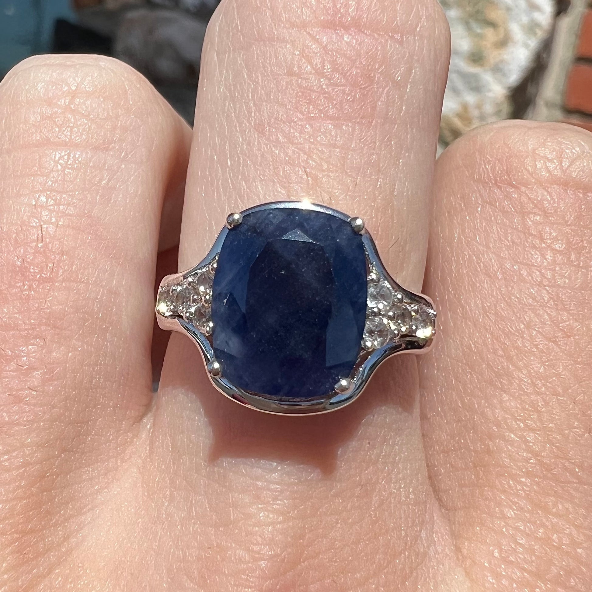A sterling silver ring set with a cushion cut blue sapphire center stone and round cut white sapphire accents.