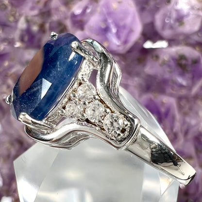 A sterling silver ring set with a cushion cut blue sapphire center stone and round cut white sapphire accents.