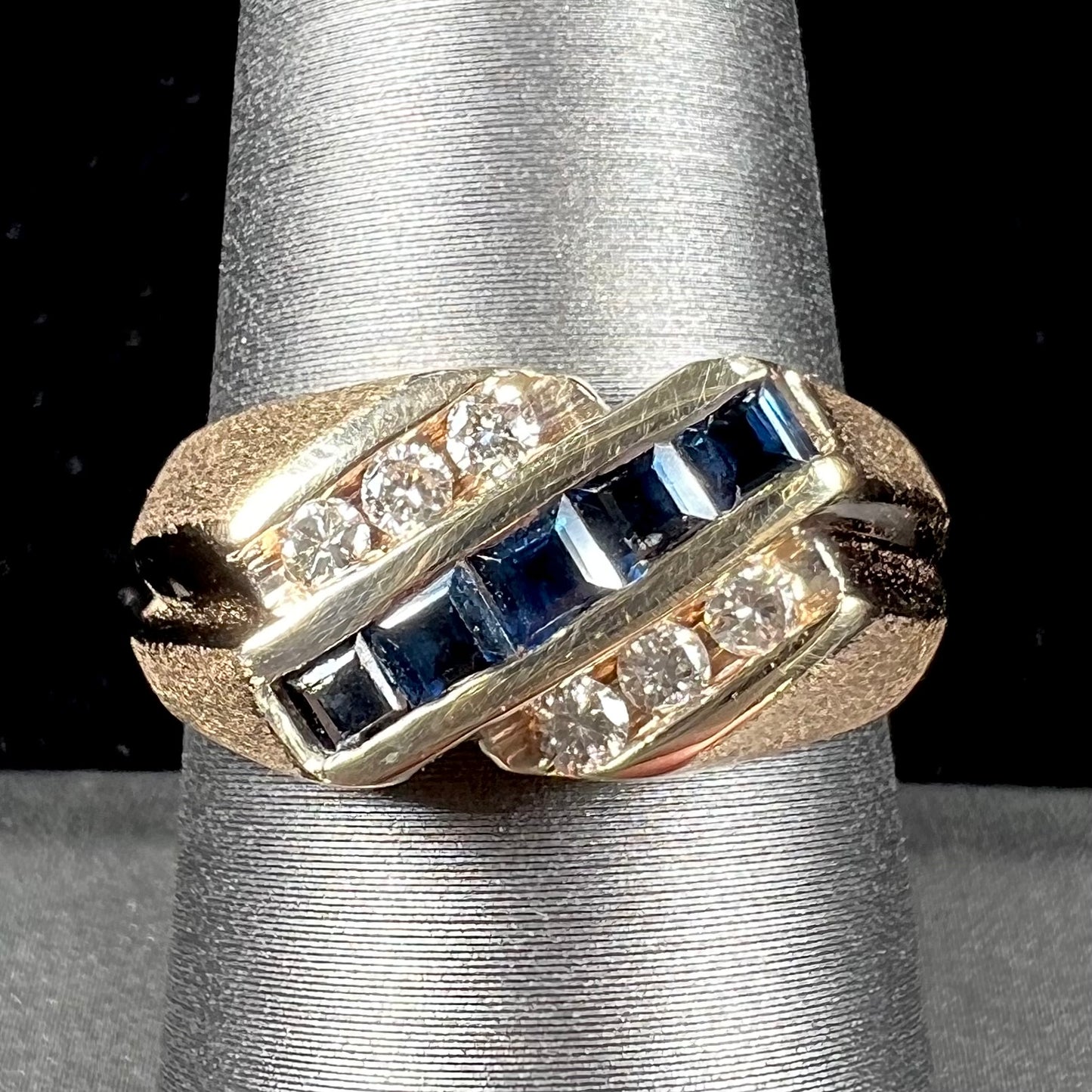 A men's yellow gold ring channel set with princess cut blue sapphires and diamonds.