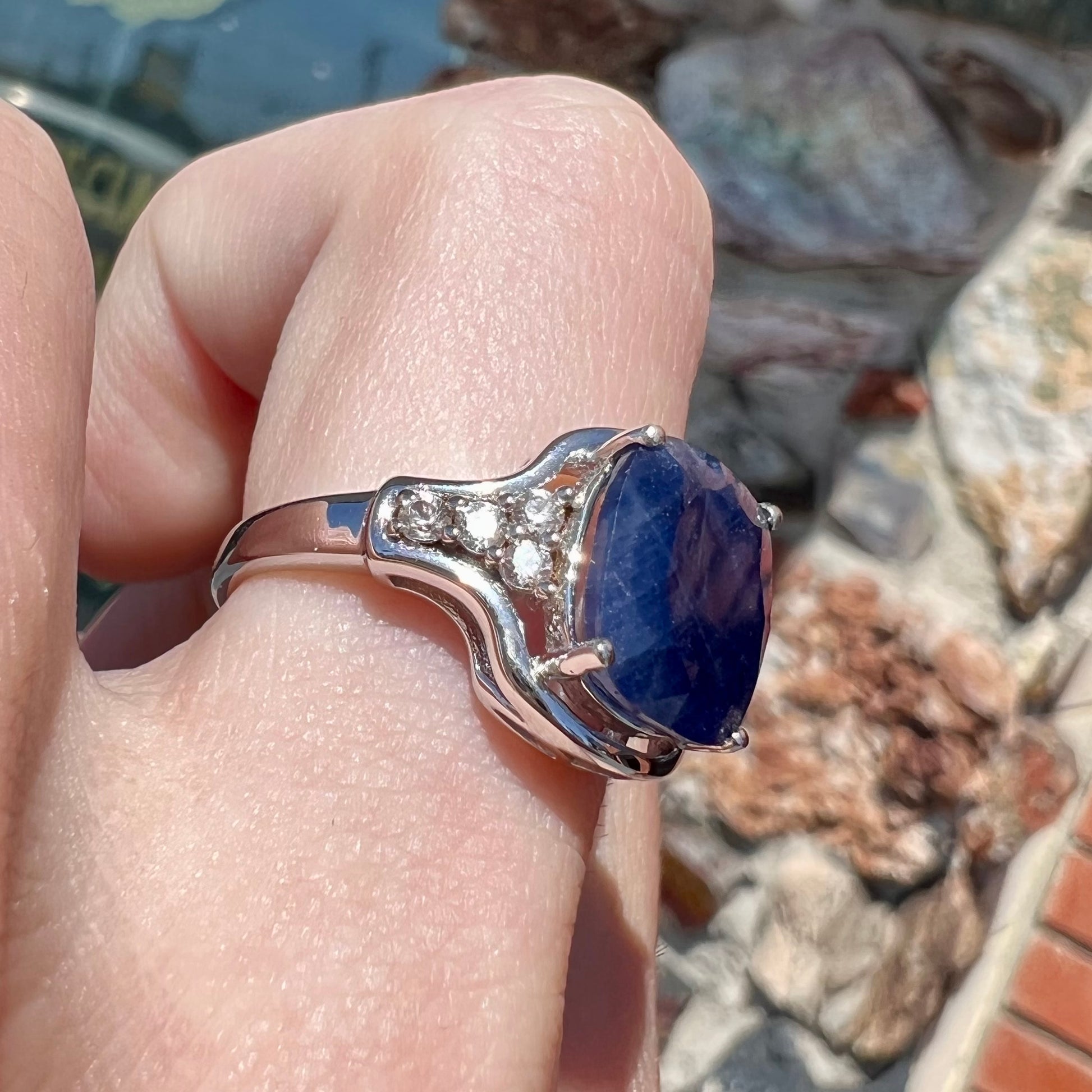 A sterling silver ring set with a cushion cut blue sapphire center stone and round cut white sapphire accents.