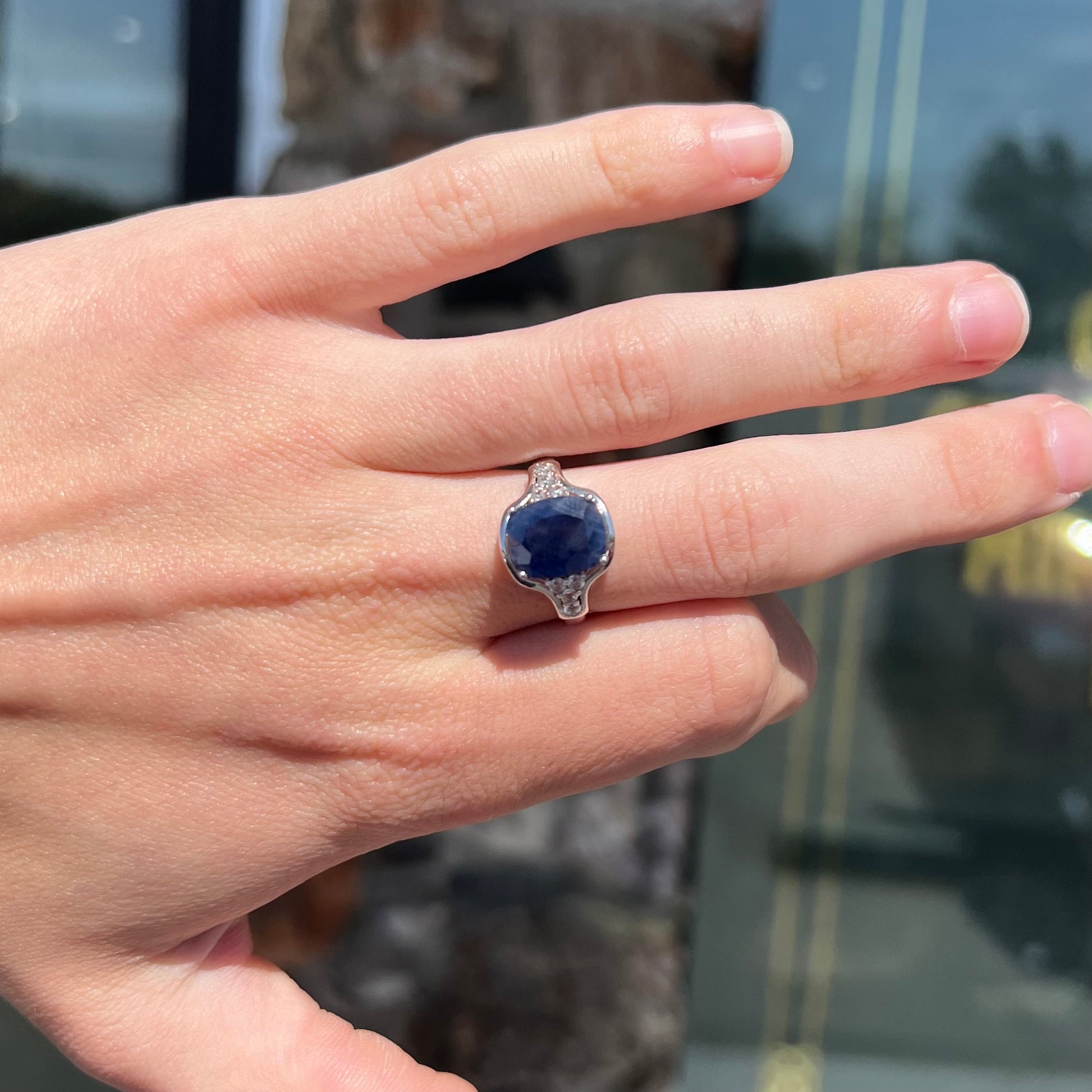 A sterling silver ring set with a cushion cut blue sapphire center stone and round cut white sapphire accents.