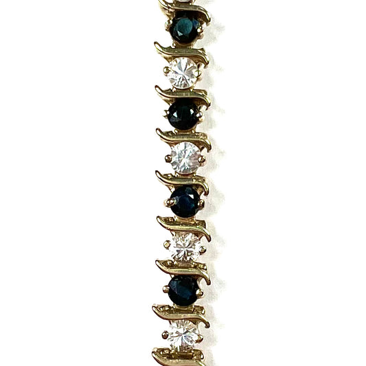A yellow gold tennis bracelet set with round midnight blue and white natural sapphires.