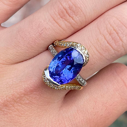 A large, oval cut blue tanzanite set in a two tone yellow and white gold diamond ring.