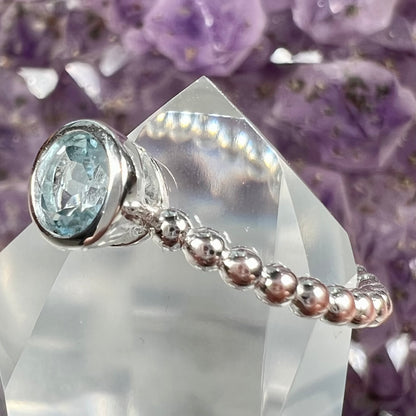A silver, bezel set, round cut sky blue topaz solitaire ring.  The band is made of connected silver balls.