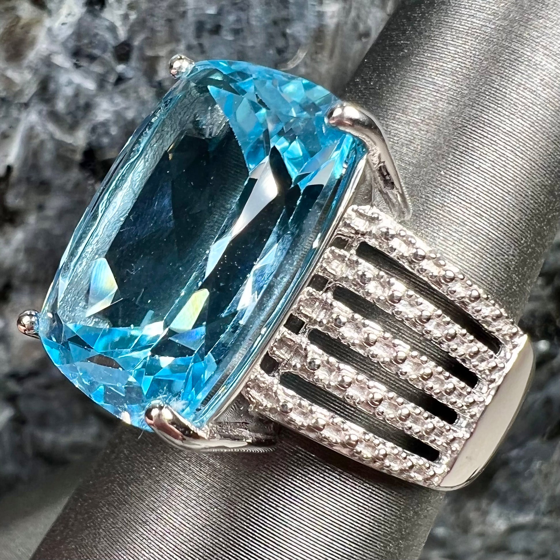 A sterling silver ring prong set with a large, cushion cut sky blue topaz stone.  The shank has been textured to mimic accent stones.
