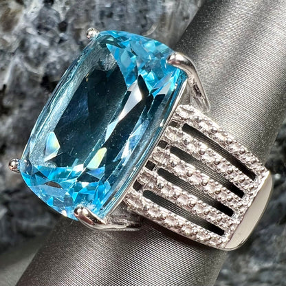 A sterling silver ring prong set with a large, cushion cut sky blue topaz stone.  The shank has been textured to mimic accent stones.