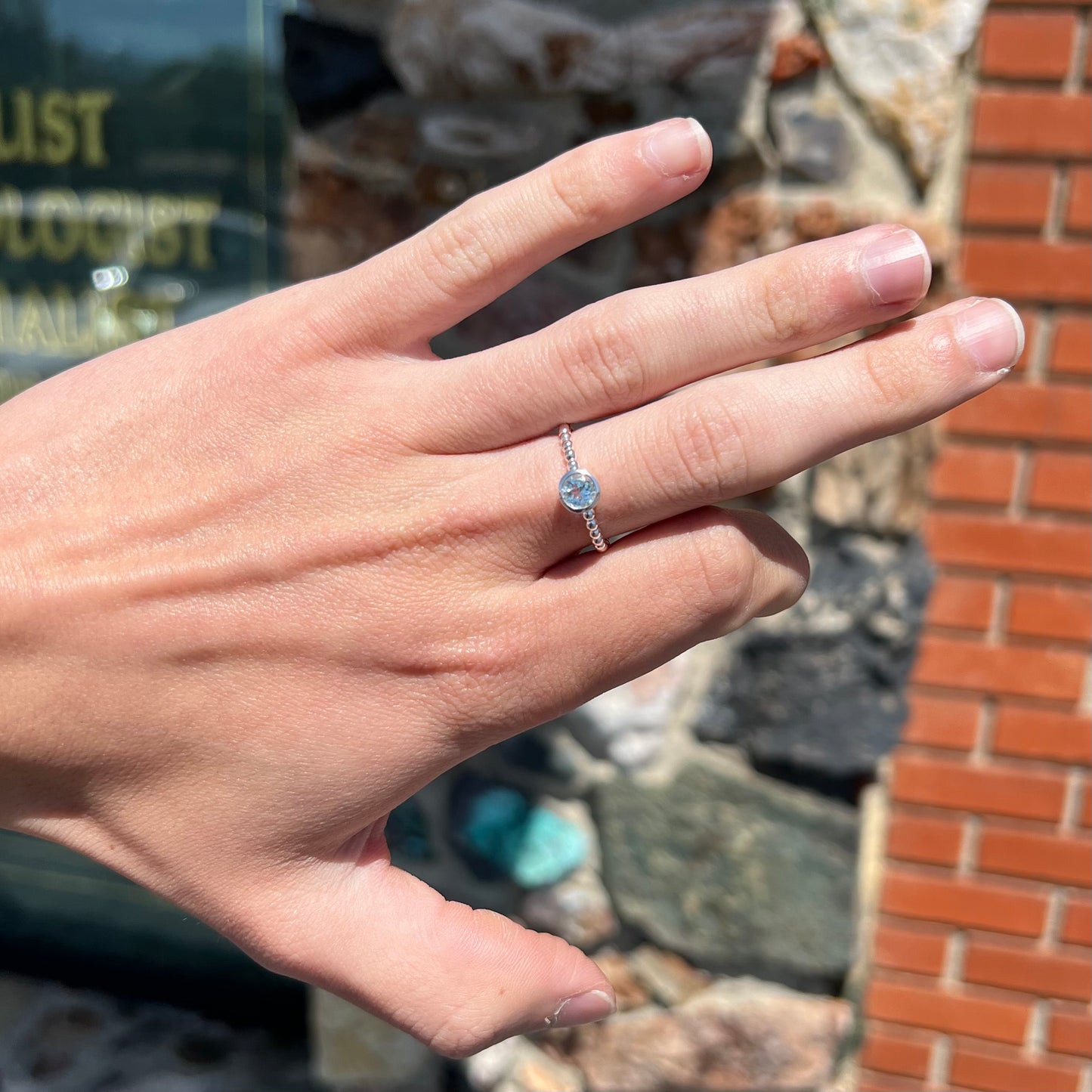 A silver, bezel set, round cut sky blue topaz solitaire ring.  The band is made of connected silver balls.