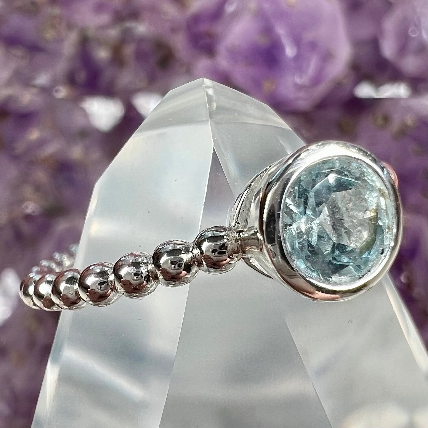 A silver, bezel set, round cut sky blue topaz solitaire ring.  The band is made of connected silver balls.