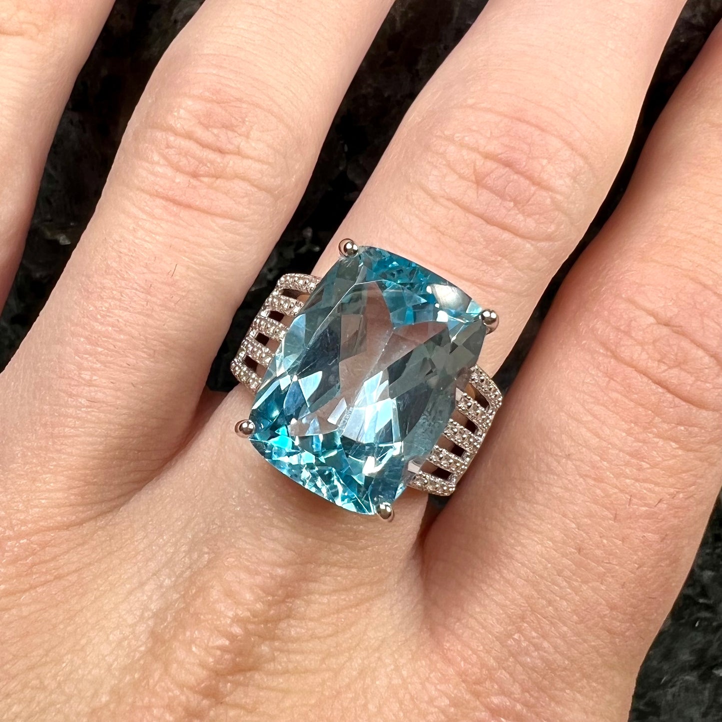 A sterling silver ring prong set with a large, cushion cut sky blue topaz stone.  The shank has been textured to mimic accent stones.