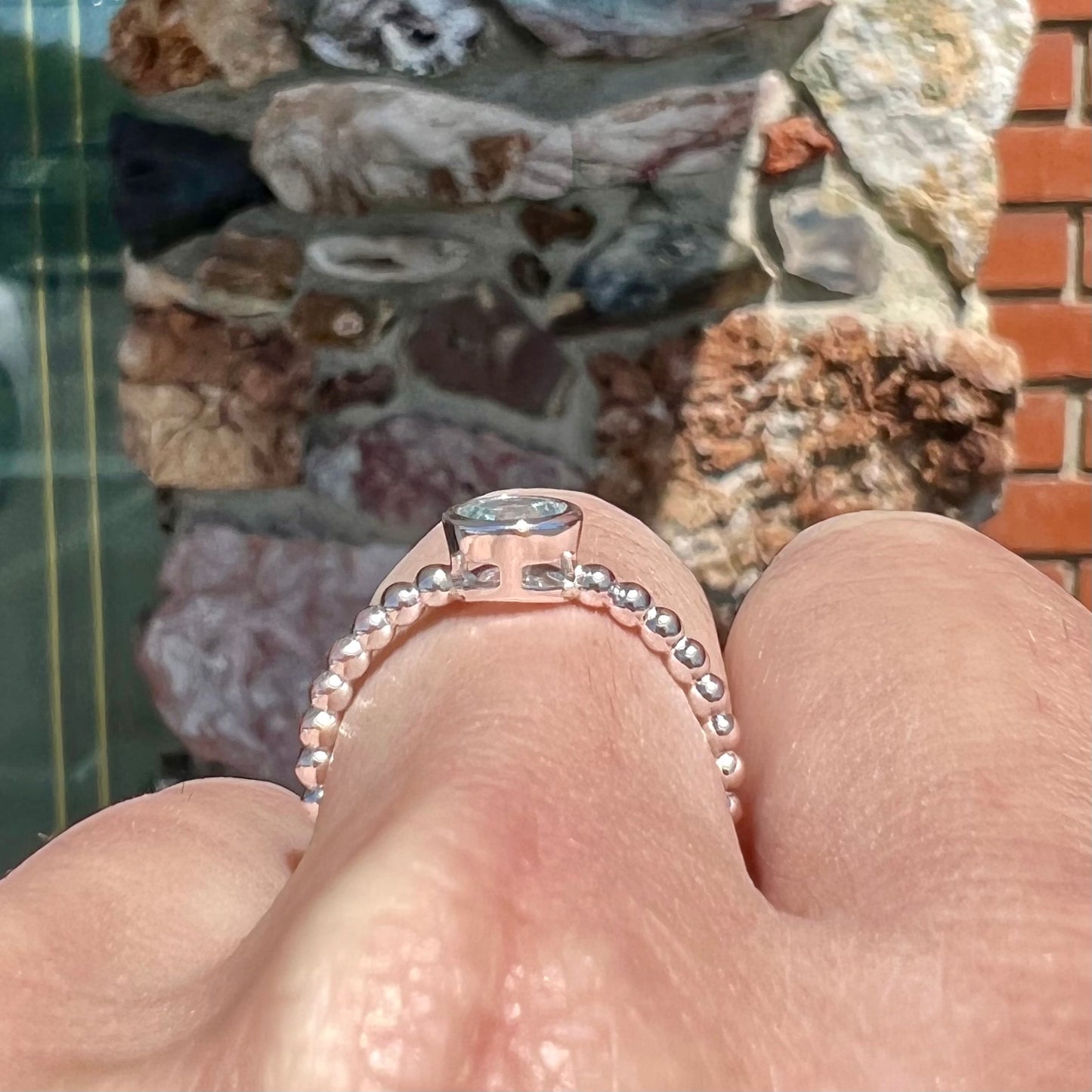 A silver, bezel set, round cut sky blue topaz solitaire ring.  The band is made of connected silver balls.