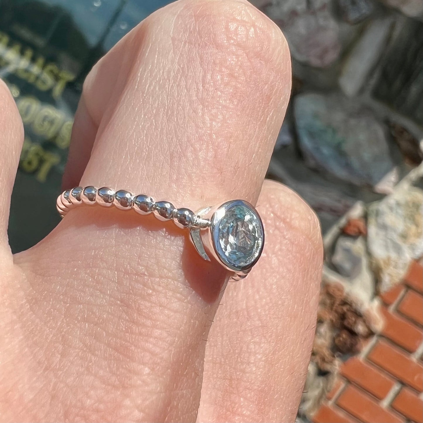 A silver, bezel set, round cut sky blue topaz solitaire ring.  The band is made of connected silver balls.