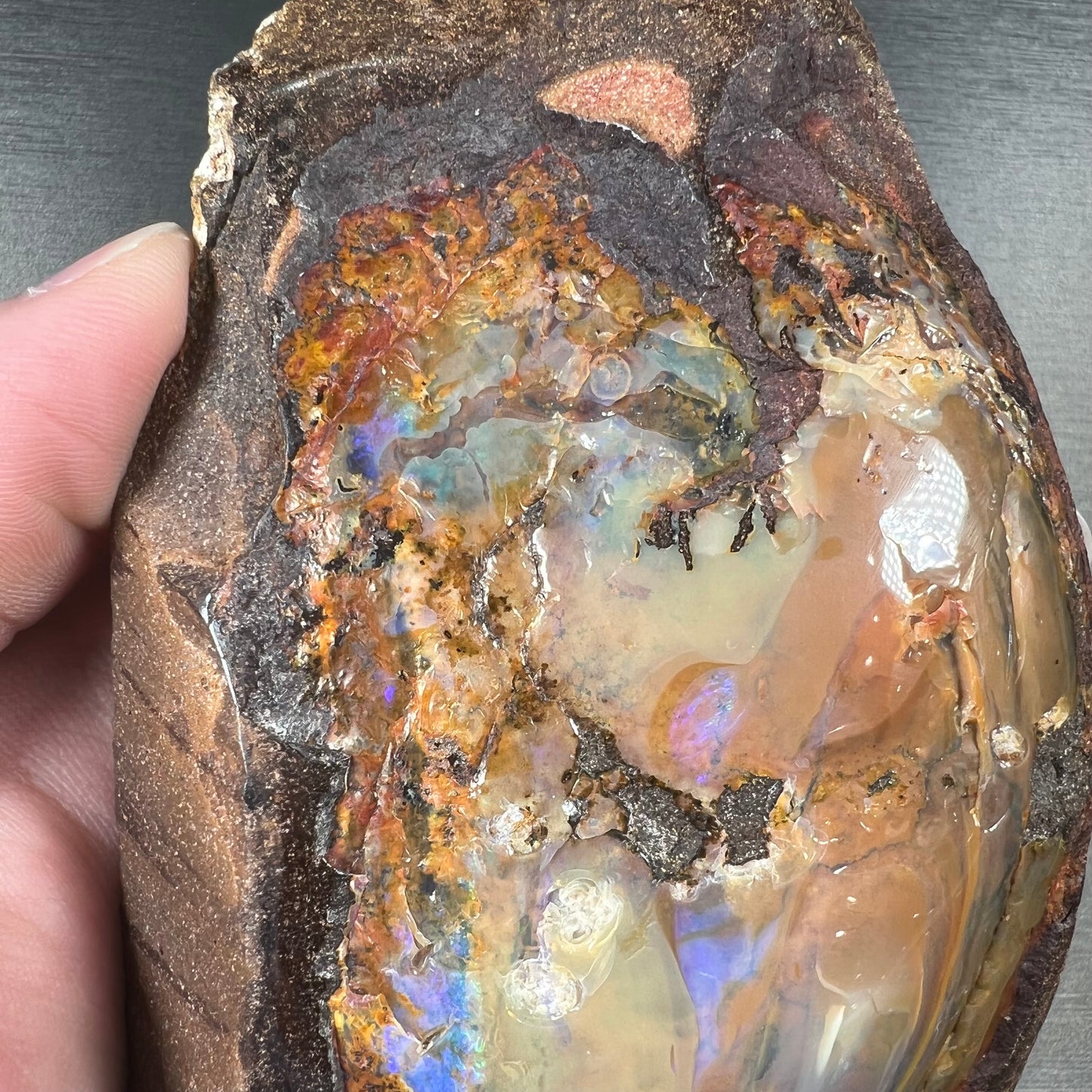 A polished Quilpie boulder opal specimen.  The stone has a stripe of bright blue, green, and purple.