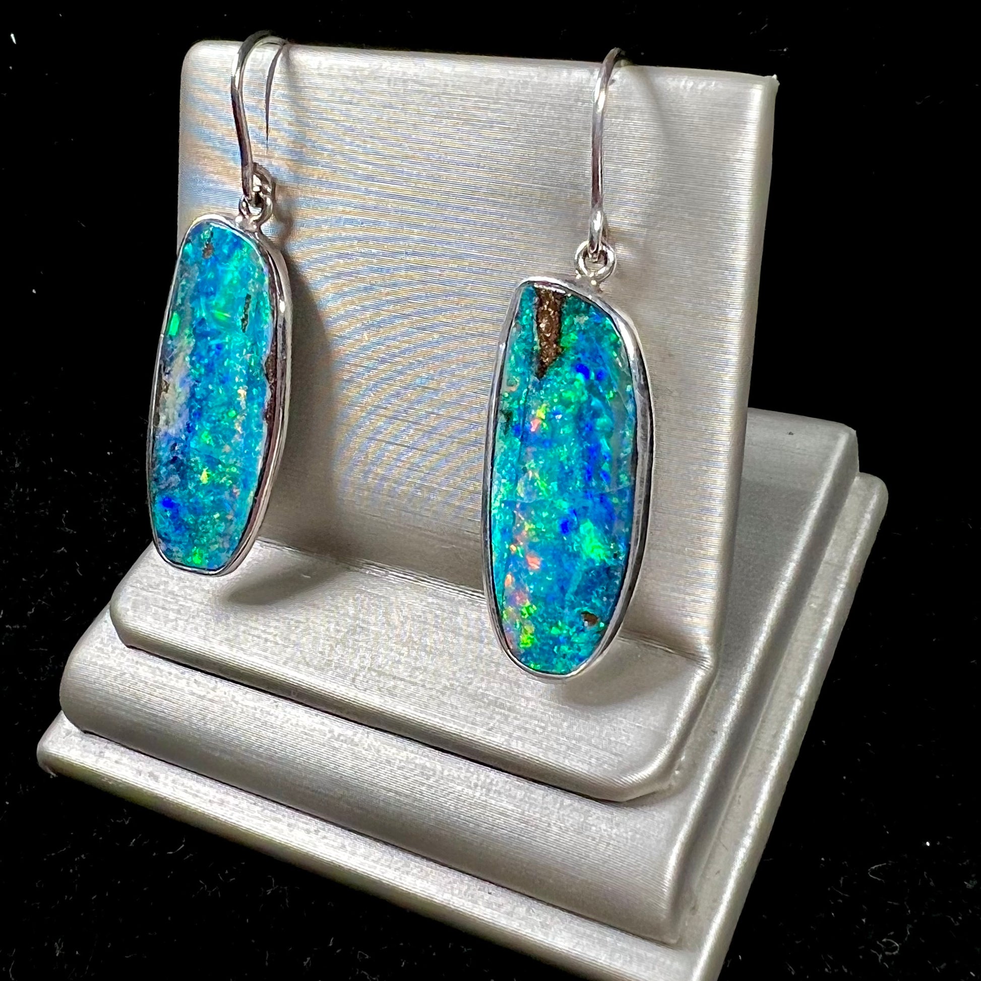 A pair of white gold boulder opal French wire dangle earrings.  The opal is predominantly glimmery blue.