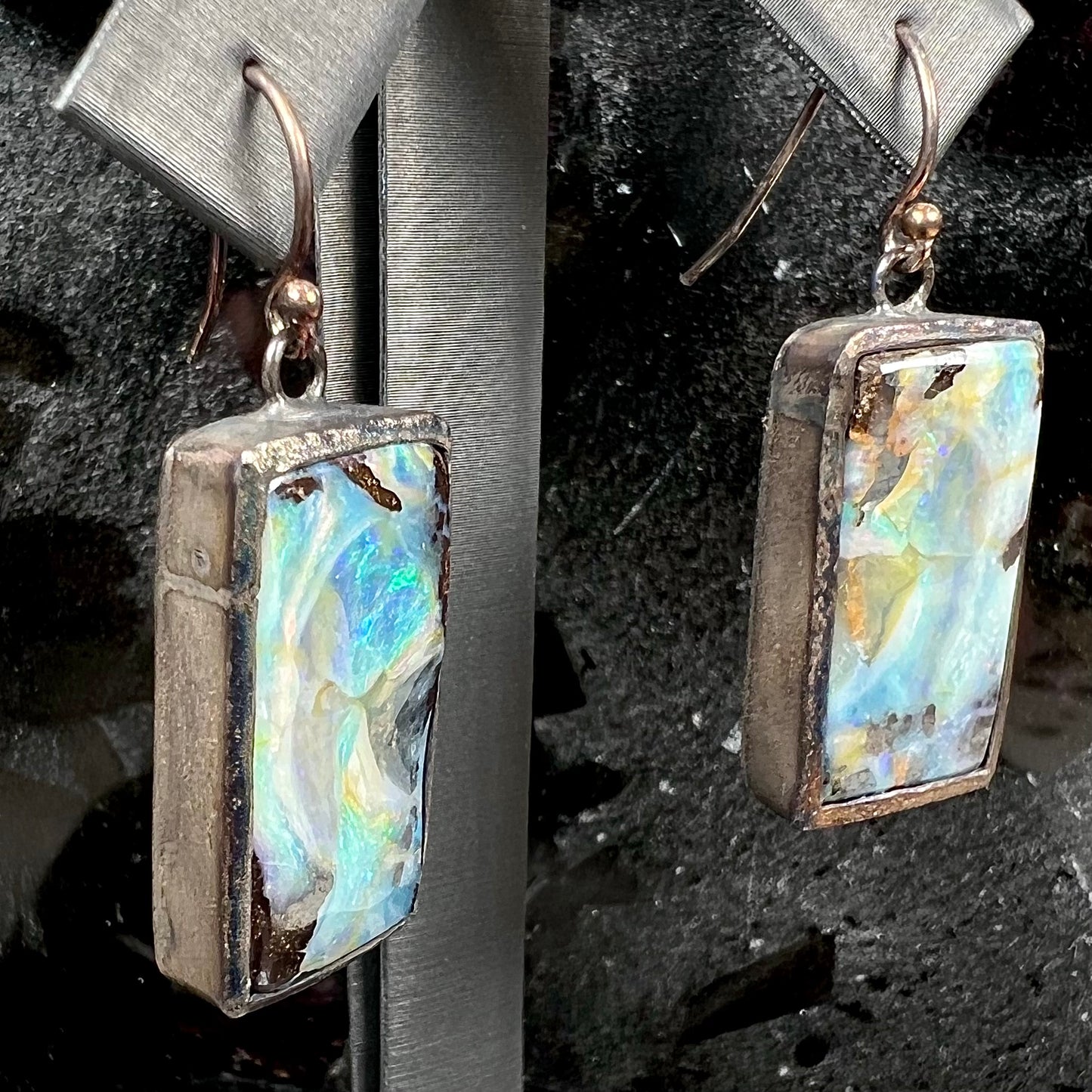 A pair of handmade sterling silver boulder opal earrings.  The earrings dangle from French wire hooks.