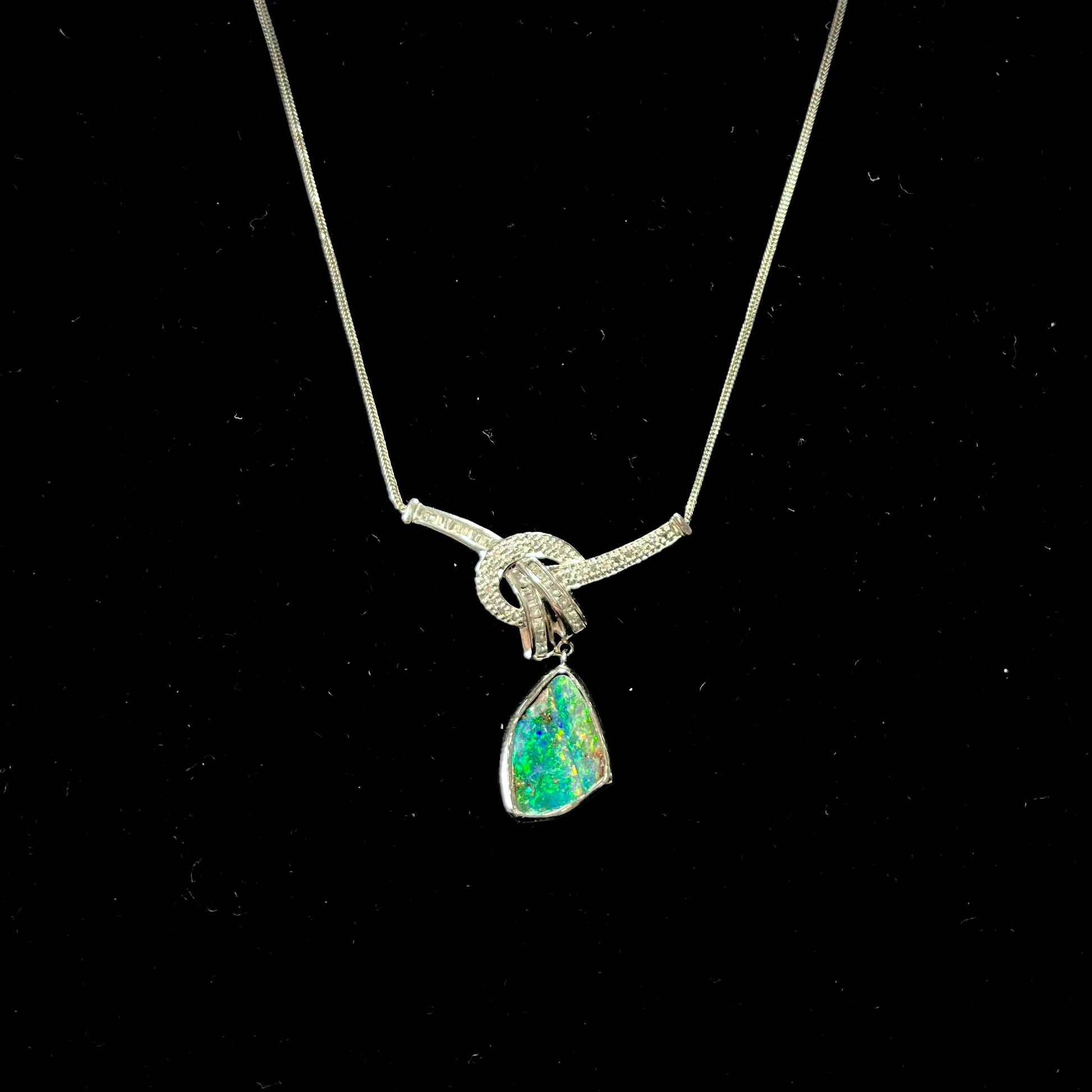 A white gold necklace set with diamonds and a dangling, bezel set boulder opal.