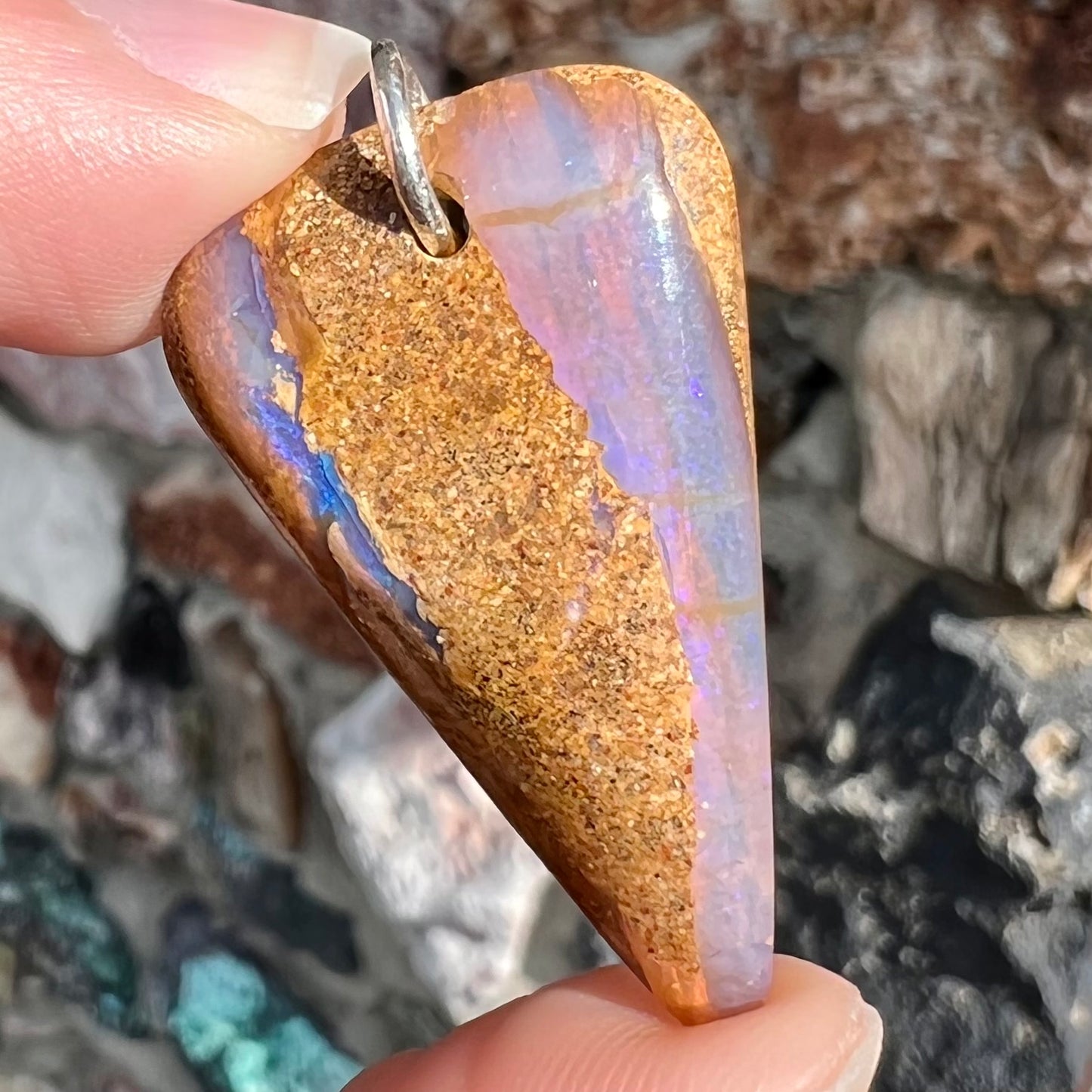 A drilled boulder opal stone with a sterling silver ring through the hole to be worn as a pendant.