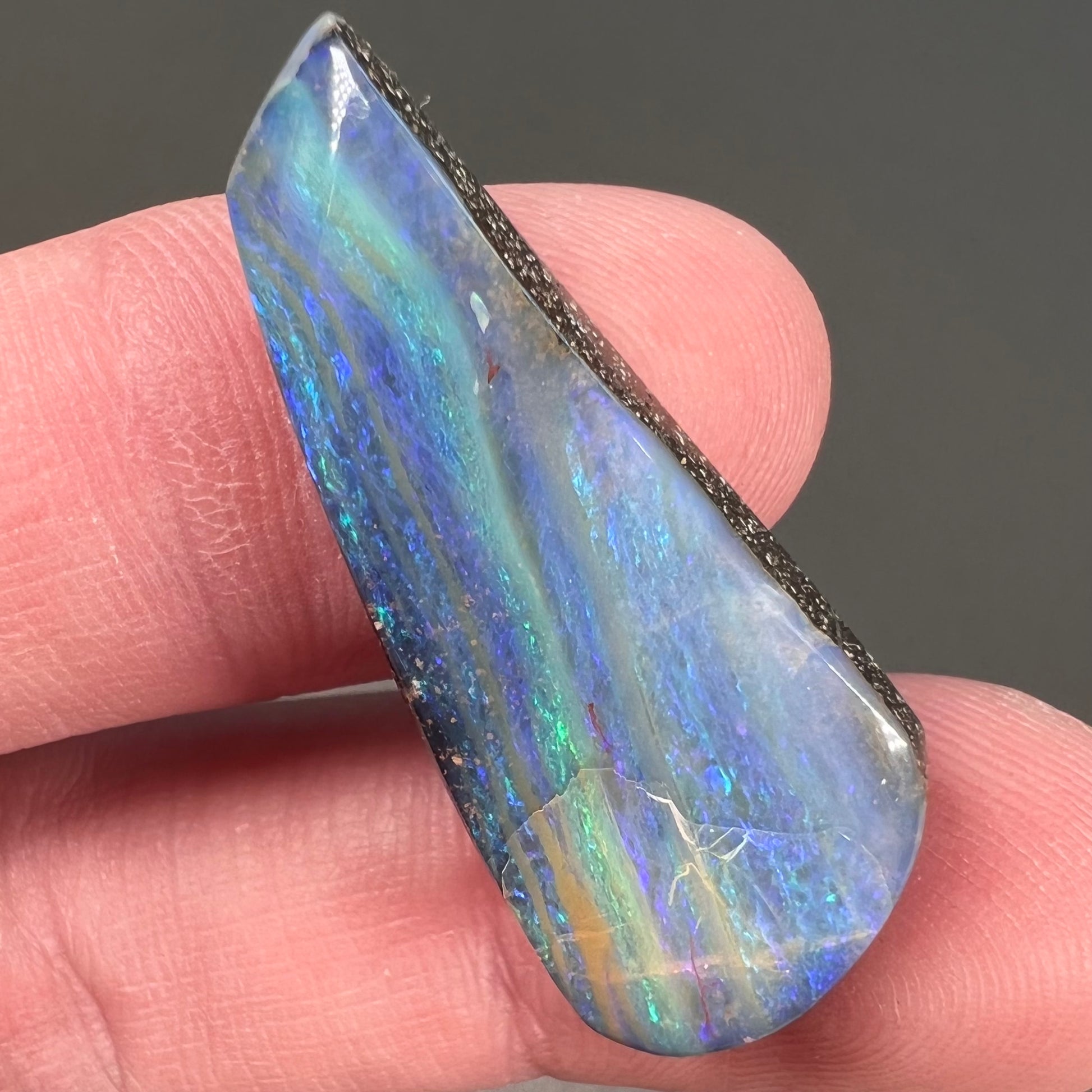 A loose, polished, freeform drop shaped boulder opal stone from Quilpie, Australia.