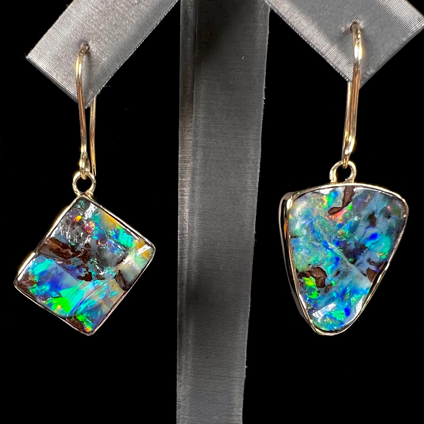 An asymmetric pair of French wire dangle yellow gold boulder opal earrings.  One opal is a square, and the other is a triangle.