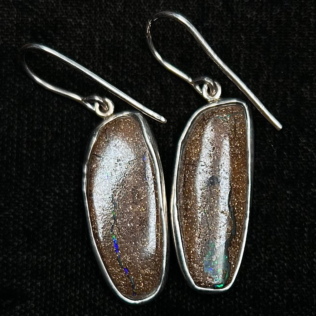 A pair of white gold boulder opal French wire dangle earrings.  The opal is predominantly glimmery blue.